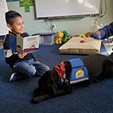 child reading a book to Canine Companions service dog