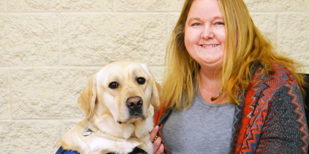 A yellow Labrador with front legs rested on woman’s lap as she sits in a wheelchair