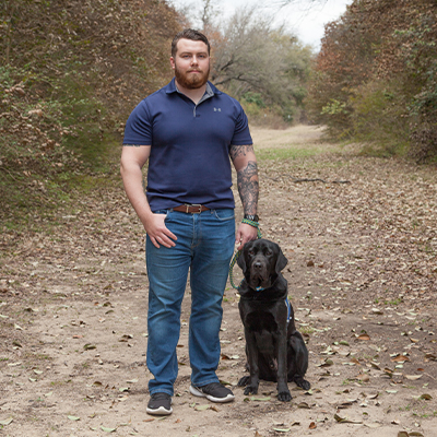 Man standing next to black Labrador sitting next to him