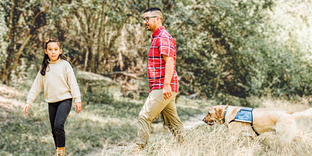 Young girl walking on trail with her father and service dog