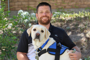 Man sitting down with his Canine Companions service dog on his lap