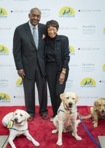 John and Joann Elliot posing on red carpet with three Canine Companions puppies