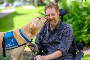 man in wheel chair being kissed by service dog