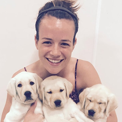 woman smiling and holding three white Labrador puppies in her arms