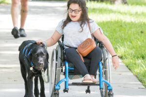 Leigh in a wheel chair walking her service dog on the sidewalk