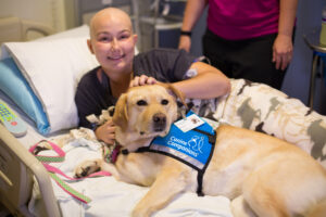 patient laying in hospital bed with Canine Companions service dog laying by their side