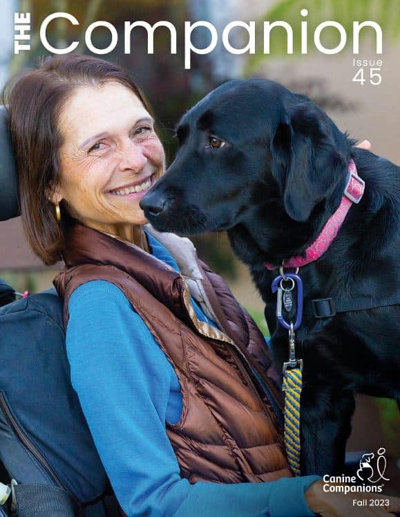 The cover of the The Companion publications Fall 2023 featuring a smiling woman in a motorized wheelchair with a black lab service dog