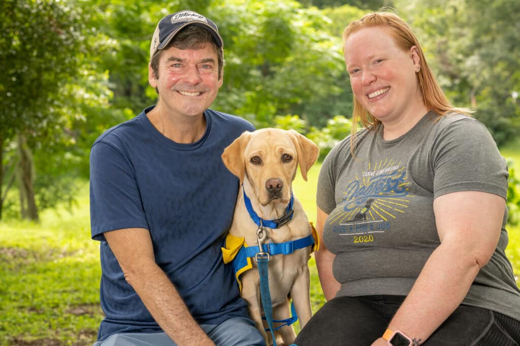 two people sitting with dog wearing a vest