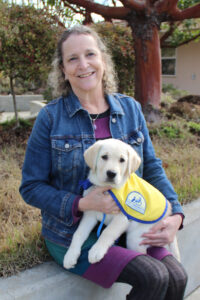 Rachel Meyer sits holding a yellow Canine Companions puppy on her lap