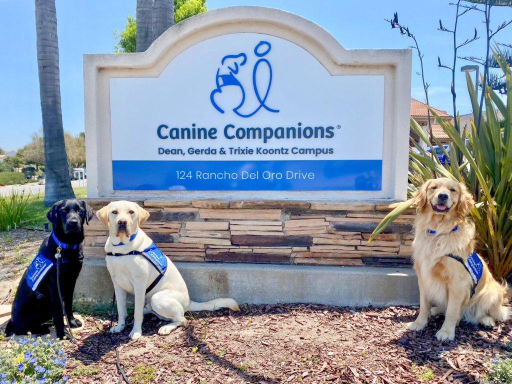 Three Canine Companions dogs sitting in front of the Southwest Region campus sign