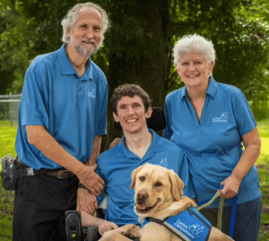 Young man in wheelchair and service dog on his lap with his parents next to him