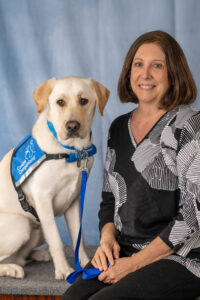 Photo of Jean and Facility Dog Fitzgerald III, a blonde dog in a blue service vest.